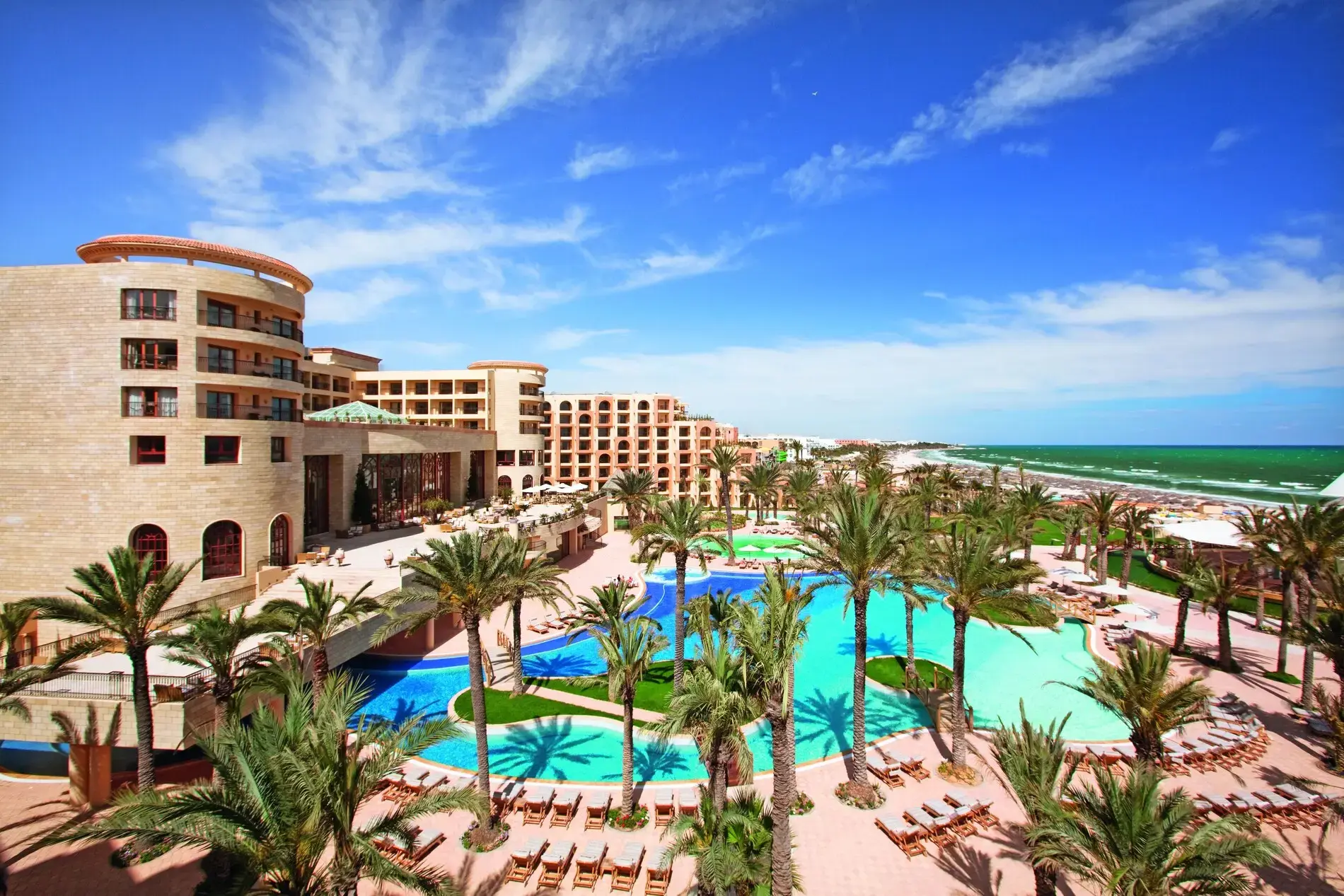 Сградите на хотела над басейните и палмовата градина през деня – Mövenpick Resort & Marine Spa Sousse, Сус