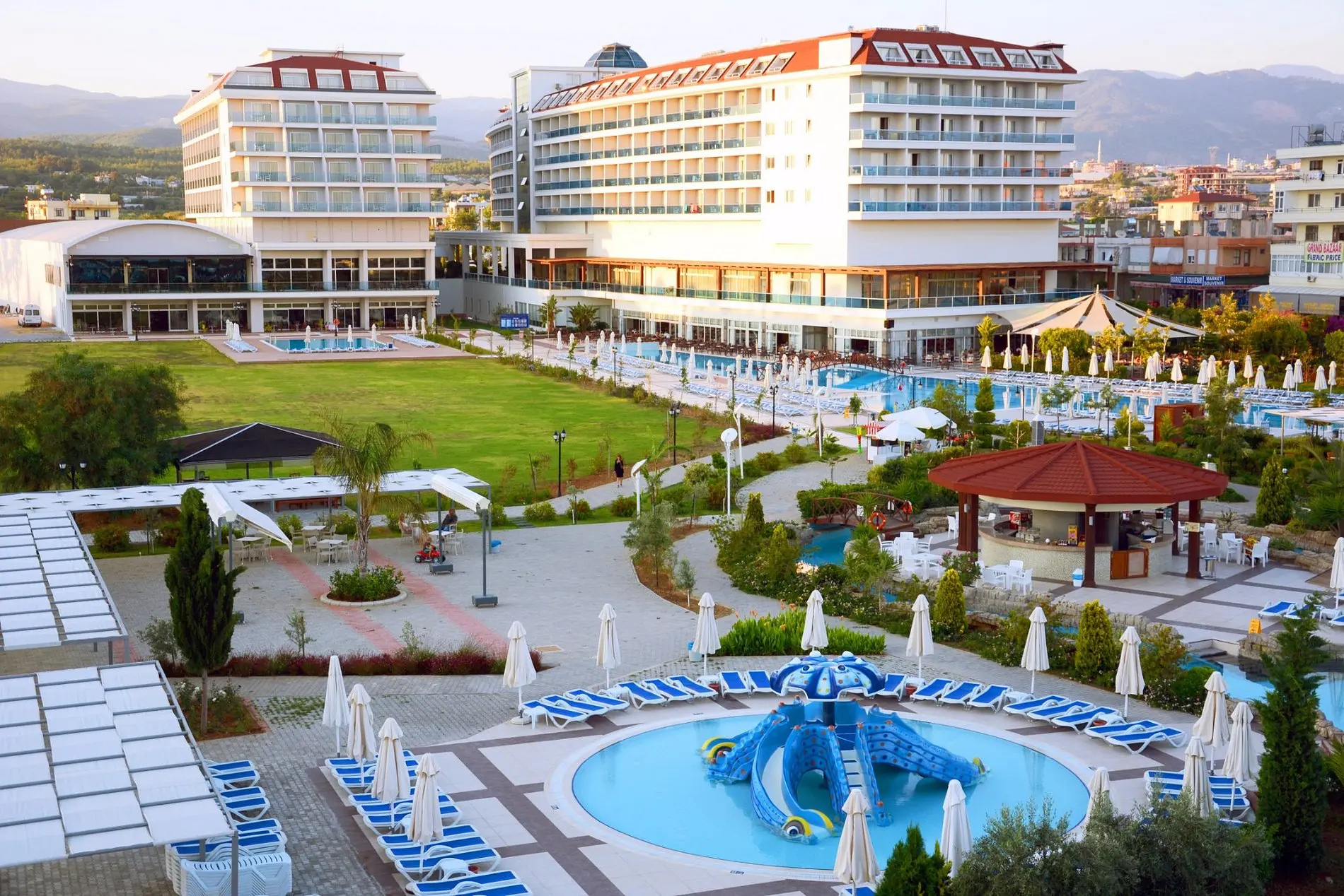 Хотелски корпуси, басейн с водна пързалка и зелена морава от високо – Kahya Resort Aqua & SPA, Алания