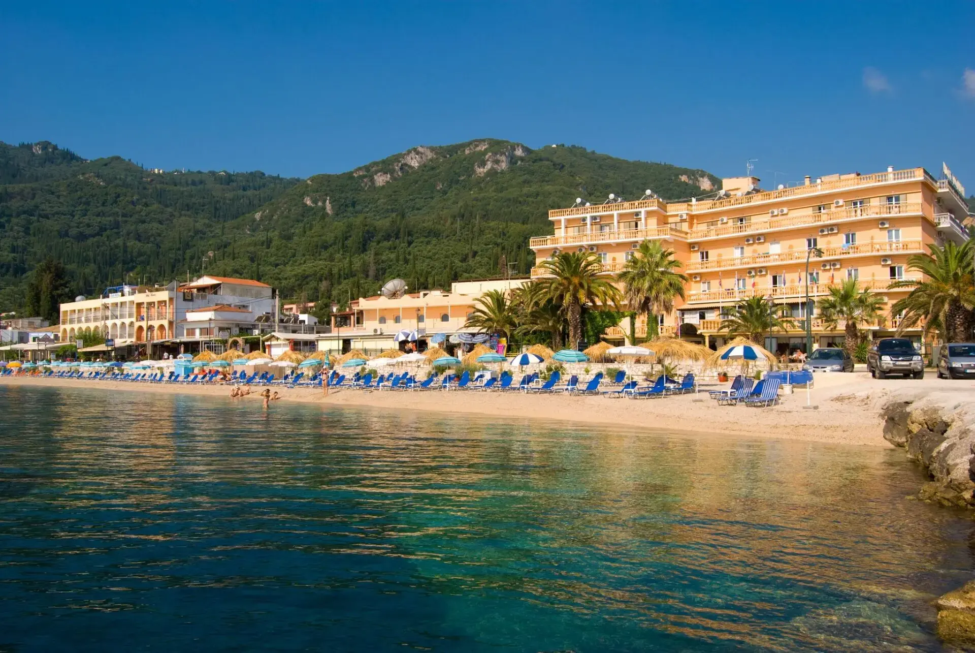 Хотелът на брега на тюркоазения залив с планини зад него – Potamaki Beach Hotel, Корфу