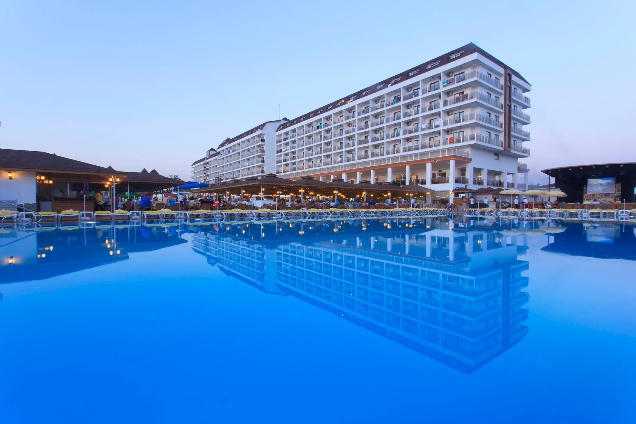 Голям външен басейн със синя вода и отражение на главната сграда – Eftalia Splash Resort, Алания