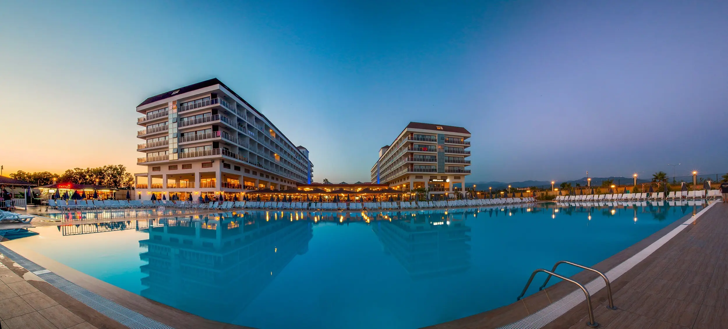 Голям басейн пред сградите на хотела, осветени по здрач – Eftalia Aqua Resort, Алания