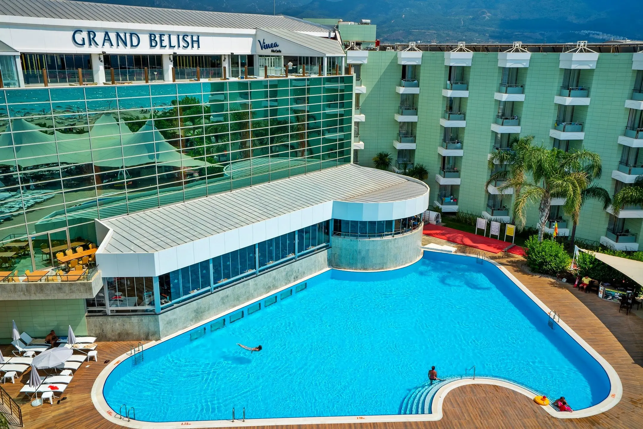 Остъклената сграда с надпис Grand Belish и голям открит басейн – Grand Belish Hotel, Кушадасъ