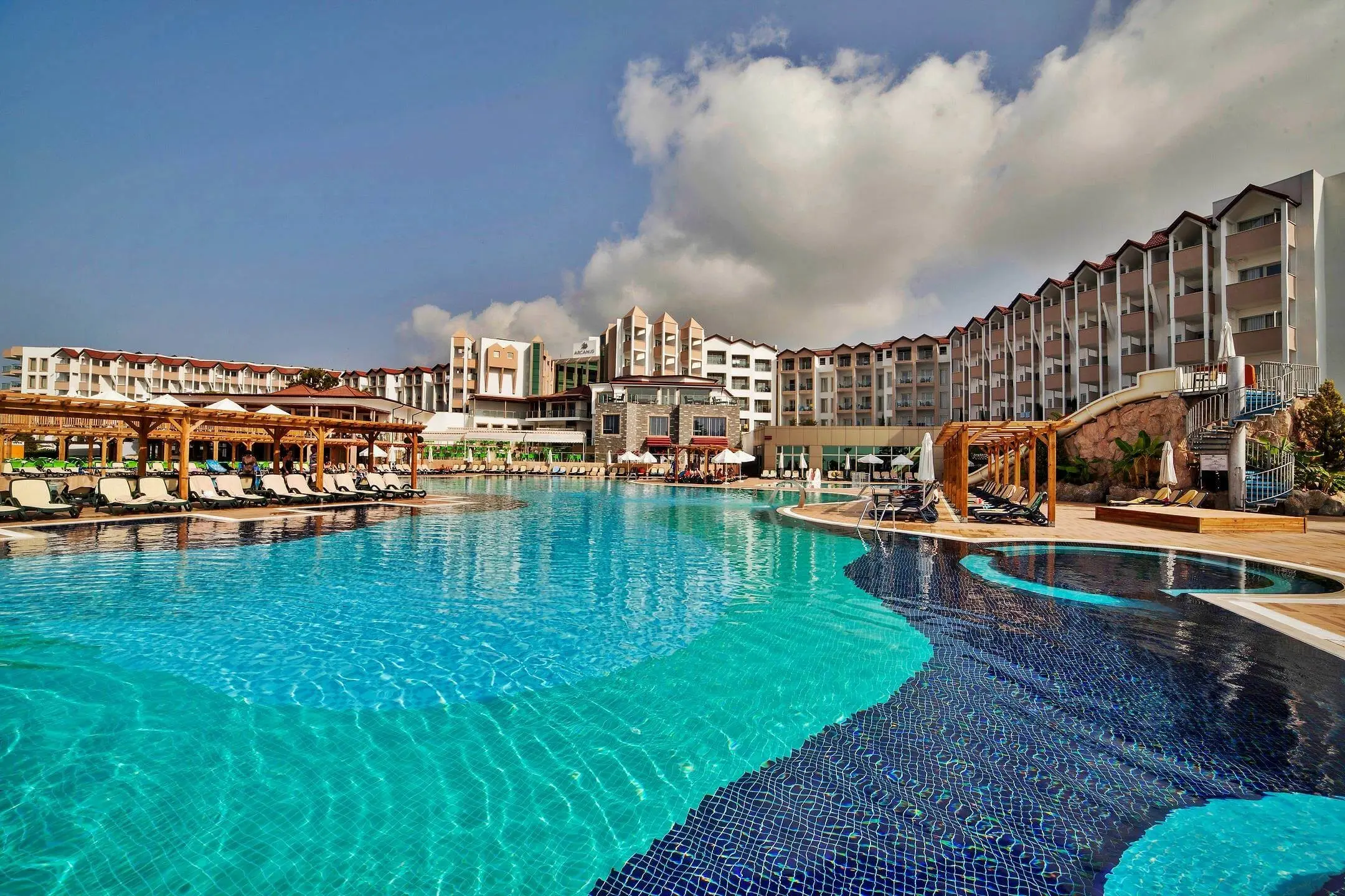 Голям басейн с извита форма пред хотелските сгради и шезлонги – Arcanus Hotels Sorgun, Сиде