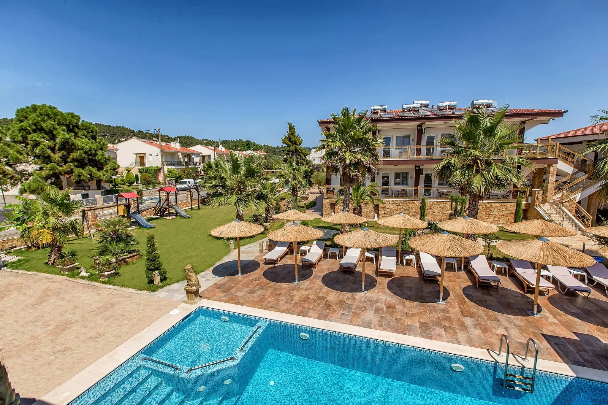 Басейн със сламени чадъри и сградата сред палми – Greek Pride Hotel Apartments, Касандра