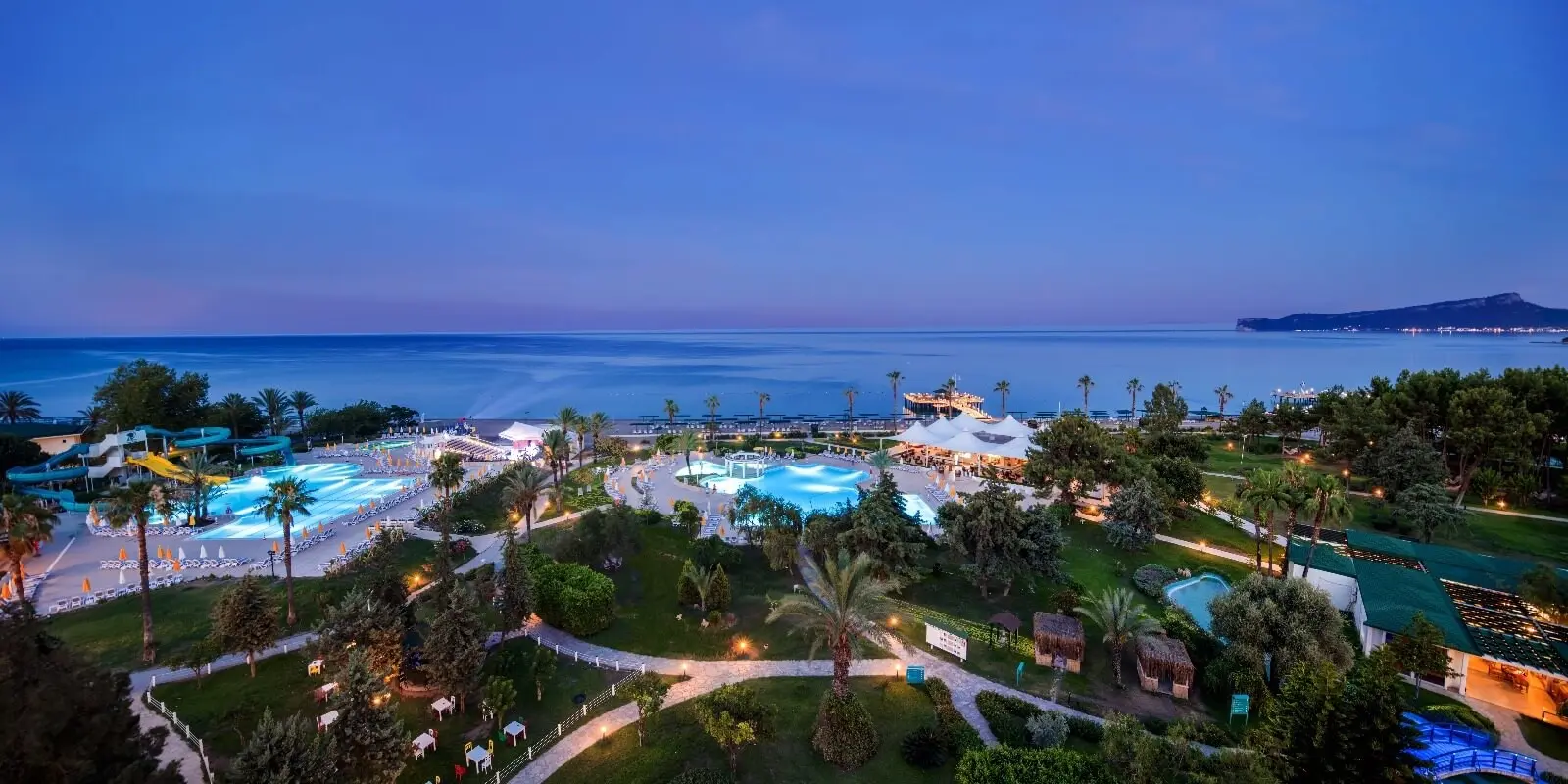 Осветени градини и басейни по здрач с изглед към морето – Mirage Park Resort, Кемер