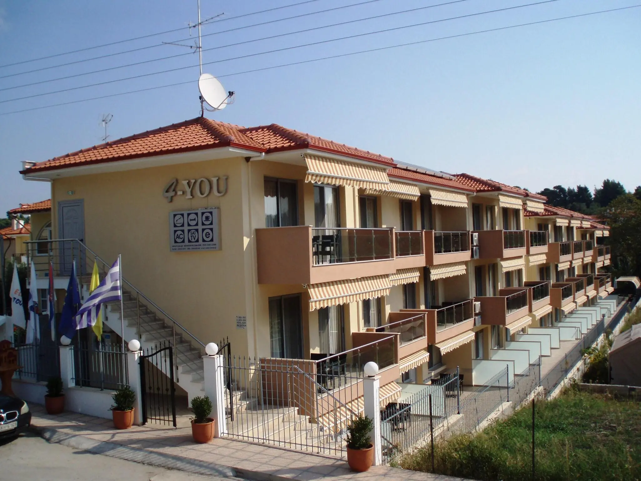 Сградата на хотела с балкони и знамена на входа – 4-You Hotel & Apartments, Ситония