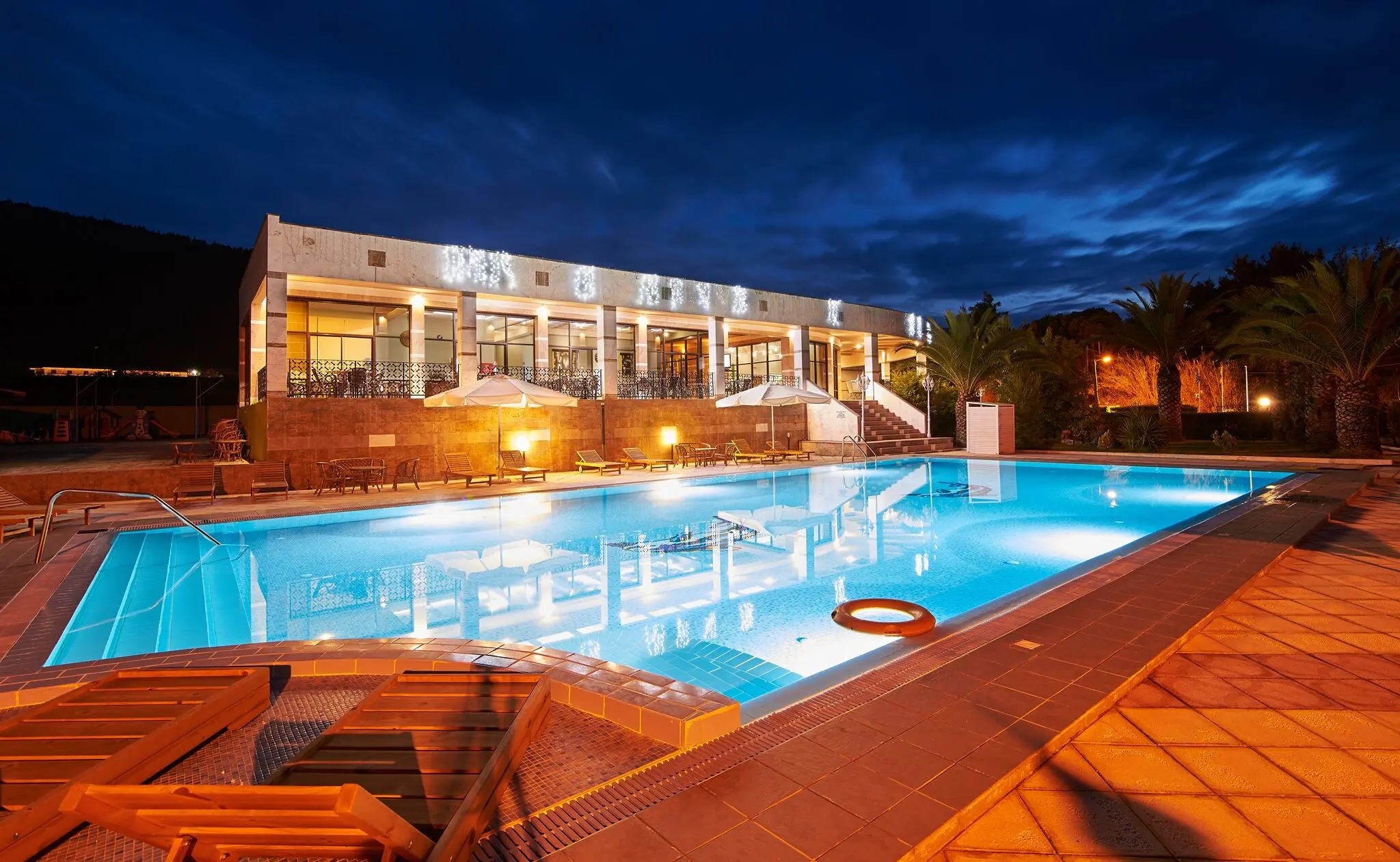 Осветеният басейн и терасата пред сградата на хотела вечер – Rema Hotel, Ситония